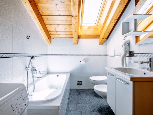 A modern bathroom with a skylight, a bathtub, a toilet, and a sink.