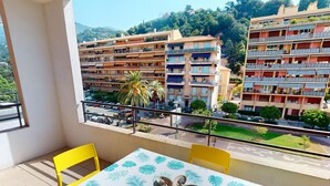 A balcony with a table and chairs, overlooking a residential area with multi-story buildings and a street. - Charming 1-BR Apt in Central Menton with Pool, Terrace & Parking (Menton)