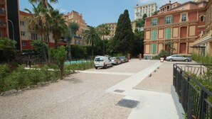 A residential street with parked cars, palm trees, and multi-story buildings with balconies. - Charming 1-BR Apt in Central Menton with Pool, Terrace & Parking (Menton)