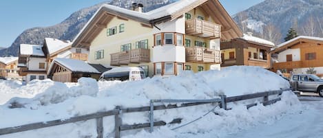 A snow-covered mountain village with traditional wooden houses, a wooden fence, and a clear blue sky.