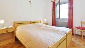 Un dormitorio con cama de madera, mesitas de noche con lámparas, una ventana con cortinas rojas y un radiador.