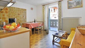 Una cocina acogedora con comedor, una pequeña mesa con mantel rojo y vista a un balcón con un edificio al fondo.