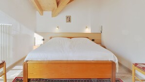 Ein Schlafzimmer mit einem hölzernen Bett, weißen Wänden und einer schrägen Decke mit freiliegenden Balken.