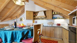 Ein Essbereich mit Tisch für vier Personen, einer Holzbalkendecke und einer Küche mit Holzschränken und Geräten.