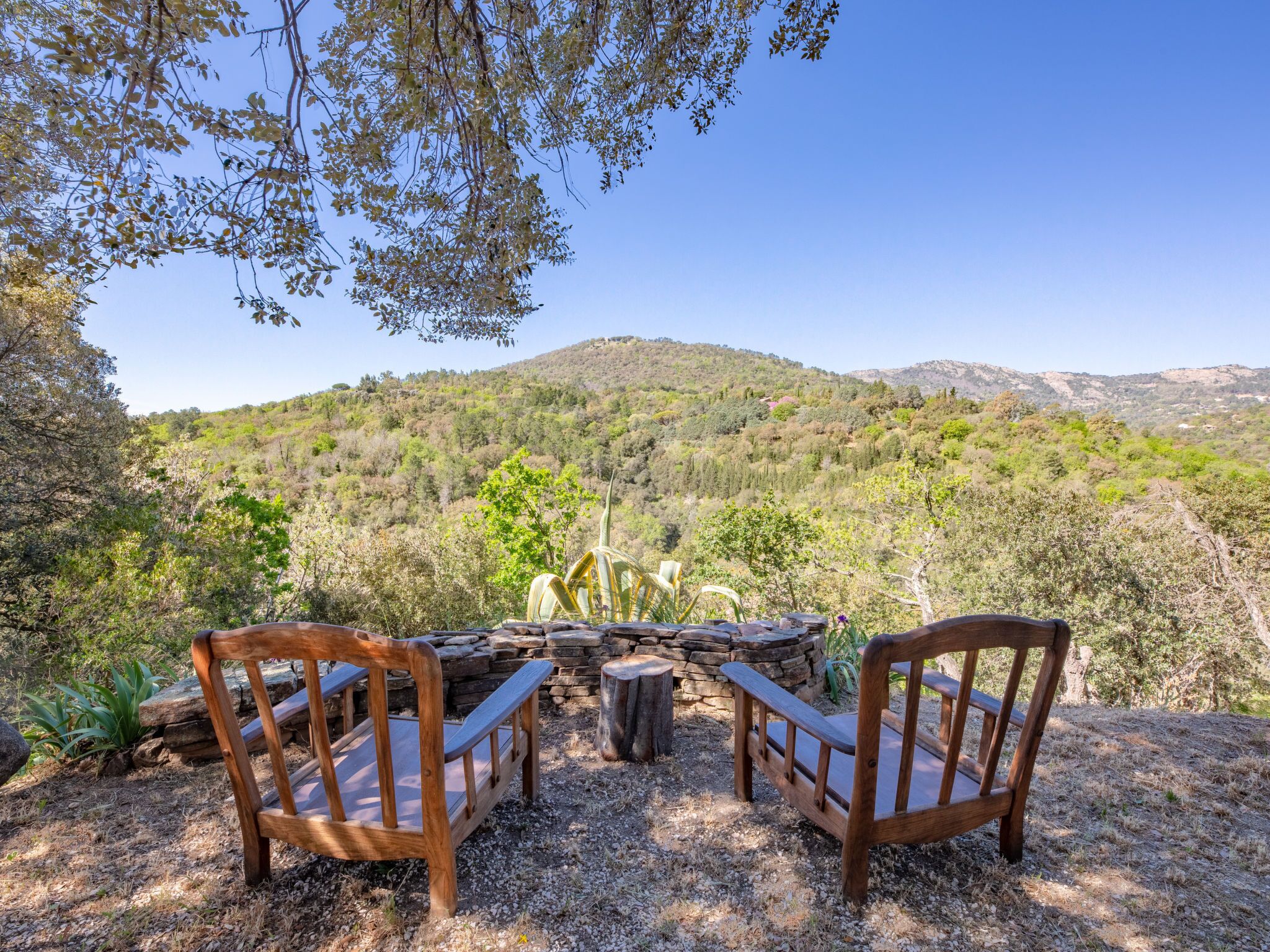 A wooden bench and table set outdoors with a view of a hilly landscape.