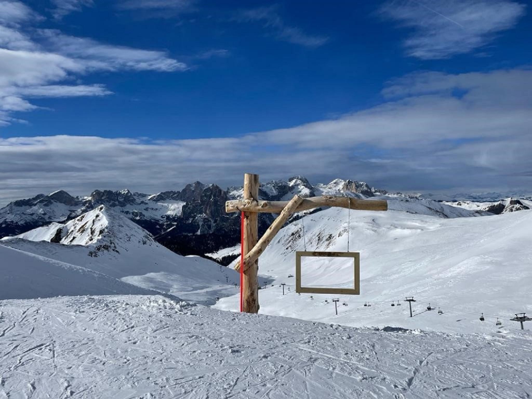 A ski lift chair suspended over a snowy mountain slope with a wooden structure in the foreground and a clear blue sky in the background.