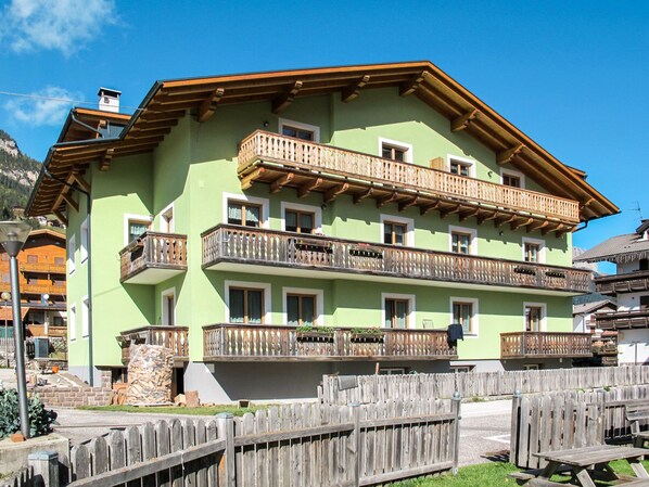 Un edificio de varios pisos con balcones, una cerca de madera y montañas al fondo.