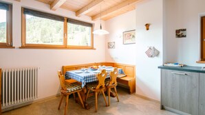 Un comedor con una mesa y sillas de madera, un radiador, y una ventana con vistas a follaje.