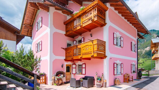 A pink building with wooden balconies and a staircase leading to the entrance.