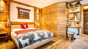 A wooden room with a bed, a wardrobe, a mirror, and a small stool.