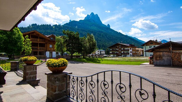 Ein Bergdorf mit traditionellen Holzhäusern, einem gepflasterten Innenhof und einem Berg im Hintergrund.