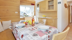 Un coin repas avec une table dressée pour deux personnes, un meuble en bois au-dessus et une fenêtre avec des rideaux.