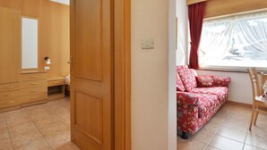 Une pièce avec une armoire en bois, un lit avec une literie à motifs floraux et une fenêtre avec des rideaux.