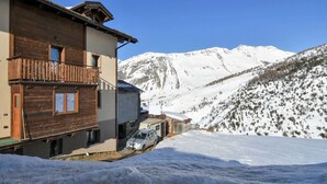 Un paisaje montañoso cubierto de nieve con un edificio de madera que tiene balcones y un coche estacionado al frente.