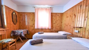 Una habitación con dos camas, una mesa con mantel floreado, una silla y paredes de madera.