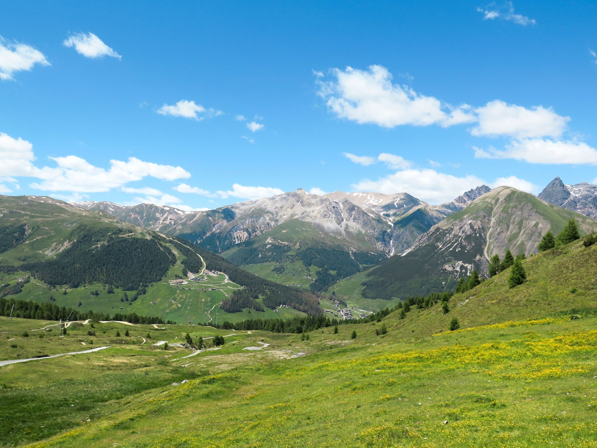 A mountainous landscape with a valley, a winding road, and scattered buildings.