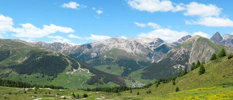 A mountainous landscape with a valley, a winding road, and scattered buildings.