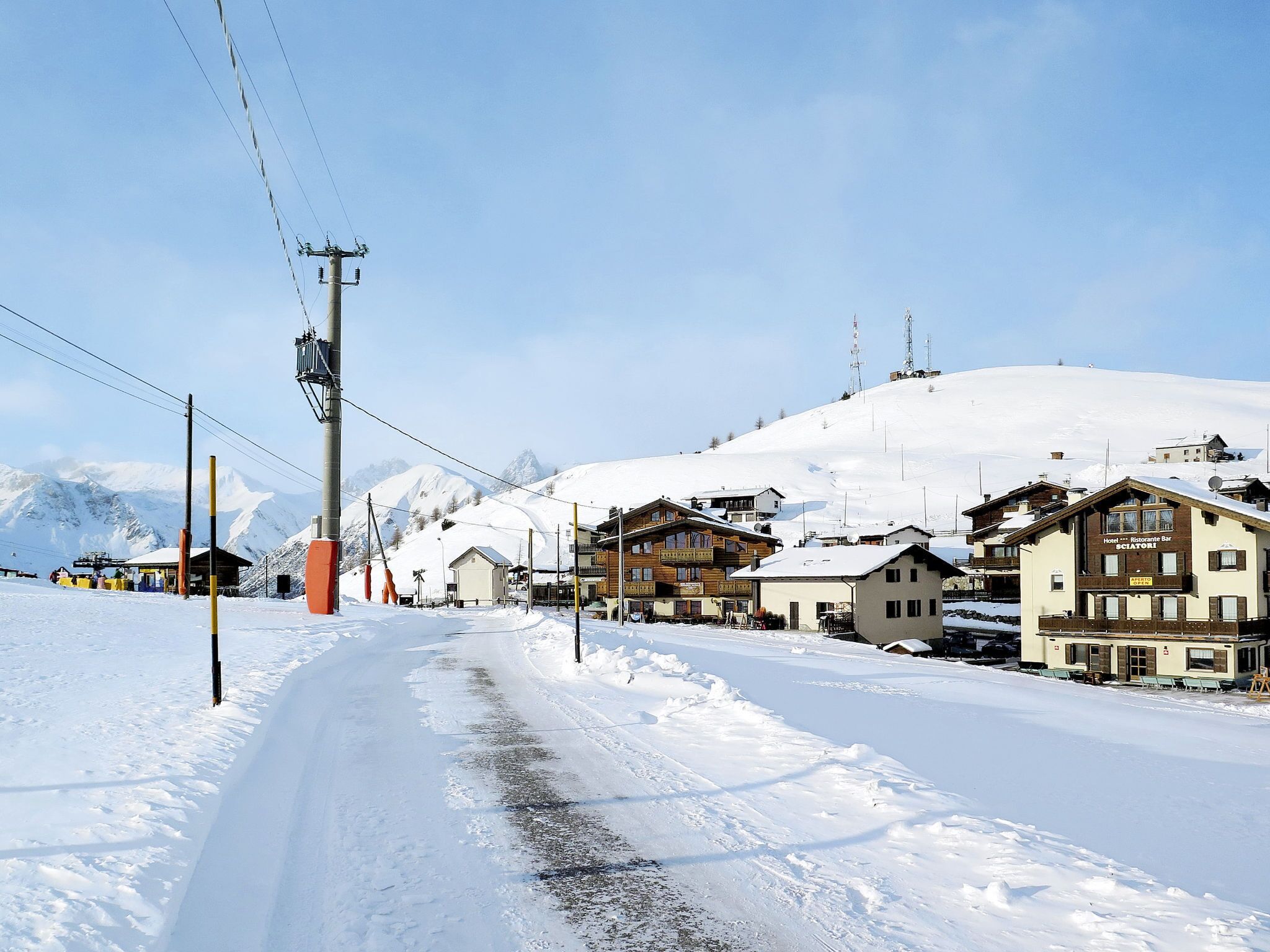 Un village enneigé avec des bâtiments en bois, un ciel dégagé et une montagne en arrière-plan.