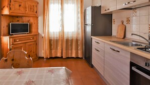 A kitchen with wooden cabinets, a refrigerator, a sink, and a television on a cabinet.