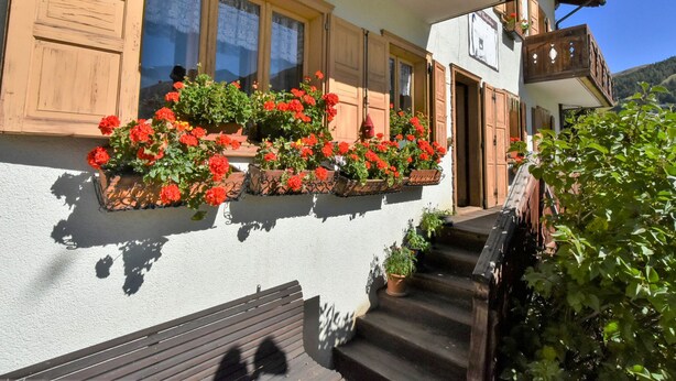 A building with a white exterior, wooden shutters, and a balcony with red flowers.