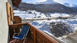 A balcony with a blue chair, wooden railing, and a view of a snowy mountain landscape.