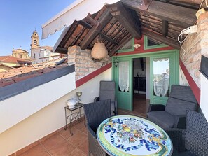 A rooftop terrace with wicker furniture, a decorative table, and a view of a church tower.