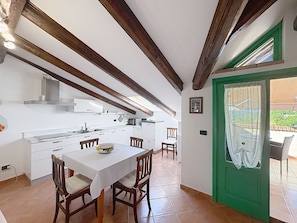 A kitchen with white cabinets, wooden beams, a dining table with chairs, and a green door leading to an outdoor area.