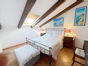 A bedroom with a bed, bedside tables, a bench, a skylight, and two wall paintings.