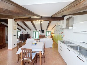 A spacious kitchen with white cabinets and a built-in sink, a dining area with a table and chairs, and exposed wooden beams on the ceiling.