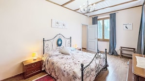 A bedroom with a bed, a nightstand, a chandelier, a window with curtains, and a door. - Il Cavaliere by Interhome (Asti)
