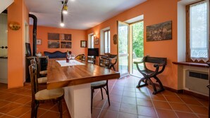 Un grand espace à manger avec une longue table en bois, plusieurs chaises et un banc. Un téléviseur est fixé au mur et une fenêtre offre une vue sur la verdure environnante.