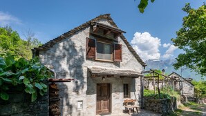 Una casa de piedra rústica con puerta de madera, un pequeño porche y un muro de piedra.