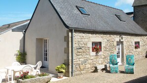 A stone building with a sloped roof, a small porch with white chairs, and a potted plant. - Avel Vor by Interhome (Saint Pol de Léon)