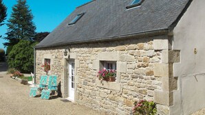 A stone building with a sloped roof, two small windows, and a door. There are outdoor chairs and potted plants visible. - Avel Vor by Interhome (Saint Pol de Léon)