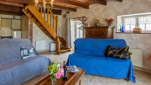 A cozy living room with a wooden staircase, a blue sofa, a coffee table with a bottle and flowers, and a kitchen area in the background. - Avel Vor by Interhome (Saint Pol de Léon)