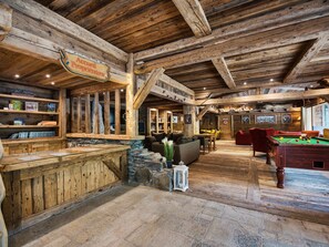 A rustic wooden interior with a billiards table, a bar area, and a cozy seating arrangement.