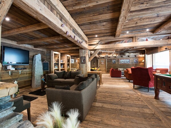 A rustic wooden interior with a sofa, red chairs, a pool table, and a television.