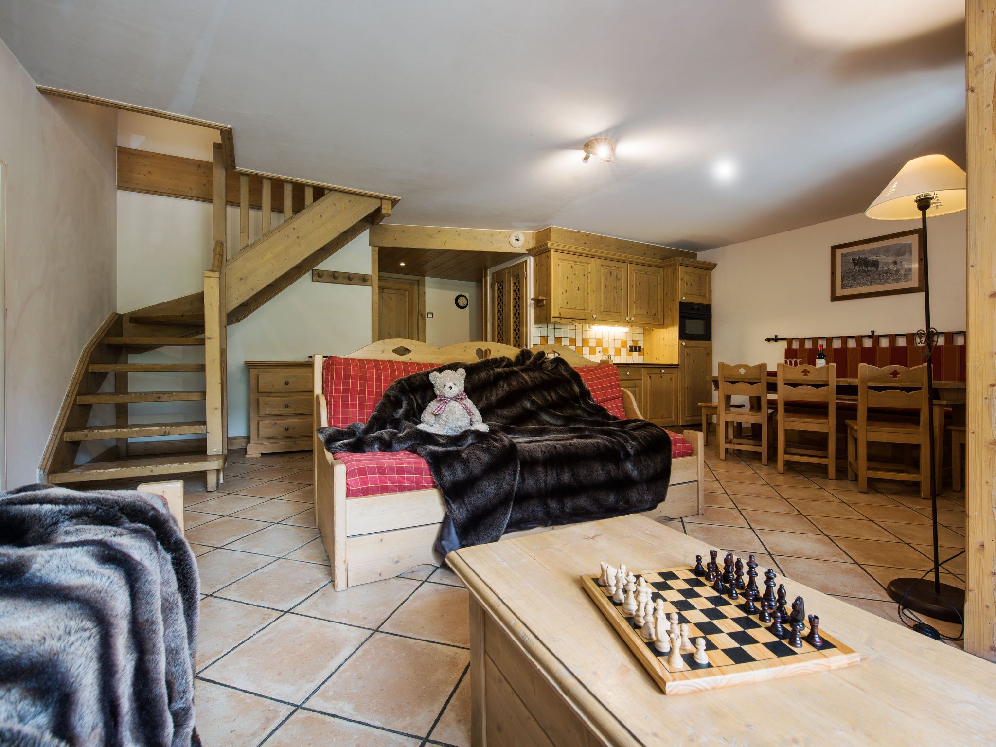 A cozy room with a bed, a wooden staircase, a kitchen area, and a chessboard.