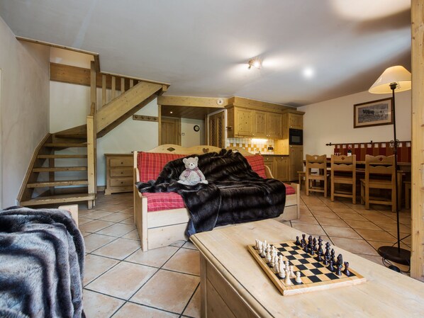 A cozy room with a bed, a wooden staircase, a kitchen area, and a chessboard.