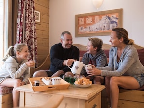 En familie på fire sidder på en træsofa i et hyggeligt rum med trævægge og et billede i ramme på væggen.