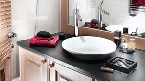 Un baño moderno con tocador de madera, un espejo grande, un lavabo blanco y zona de ducha.