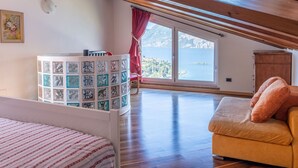A bedroom with a wooden ceiling, a bed, a red chair, a small table, and a view of a lake through a window. - Vacation home Verdin by Interhome (Malcesine)
