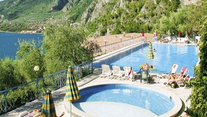 Un área de piscina con sillones de descanso y sombrillas, rodeada de vegetación y montañas.