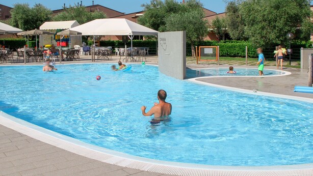 Une piscine où des gens nagent et s’amusent, entourée de parasols et de chaises longues.