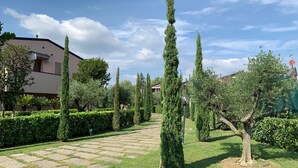 Un jardin bien entretenu, avec un chemin pavé, des haies soigneusement taillées et de grands cyprès.