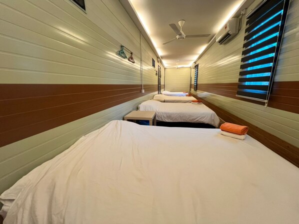 Un pasillo estrecho con tres camas alineadas a lo largo de la pared, cada una con ropa de cama blanca y toallas naranjas.