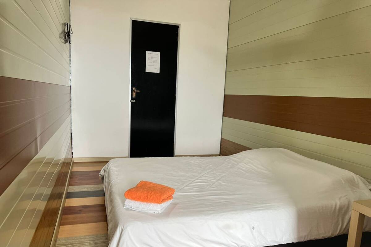 Ein Hotelzimmer mit einem Bett, Holzboden, einer schwarzen Tür und einer weißen Wand.