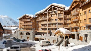 Un edificio de madera de varios pisos con balcones, niveles inferiores de piedra y una montaña cubierta de nieve al fondo.
