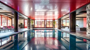 A large indoor swimming pool with clear water, surrounded by lounge chairs and stone pillars. - Le Télémark 5* by Interhome (Tignes)