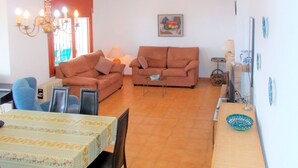 A living room with two sofas, a dining table with chairs, a chandelier, and a painting on the wall. - Vacation home Grecia by Interhome (Peñiscola)
